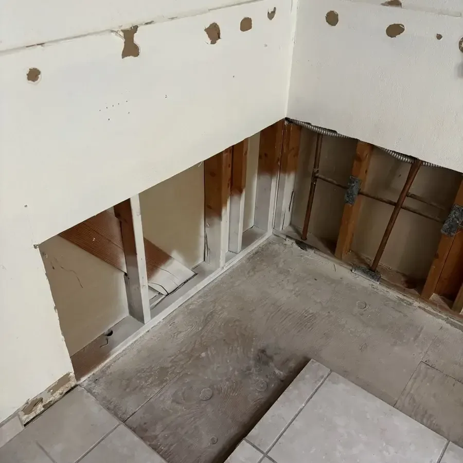 Wall cavity opened above a tile floor so the framing can dry after a leak in an home