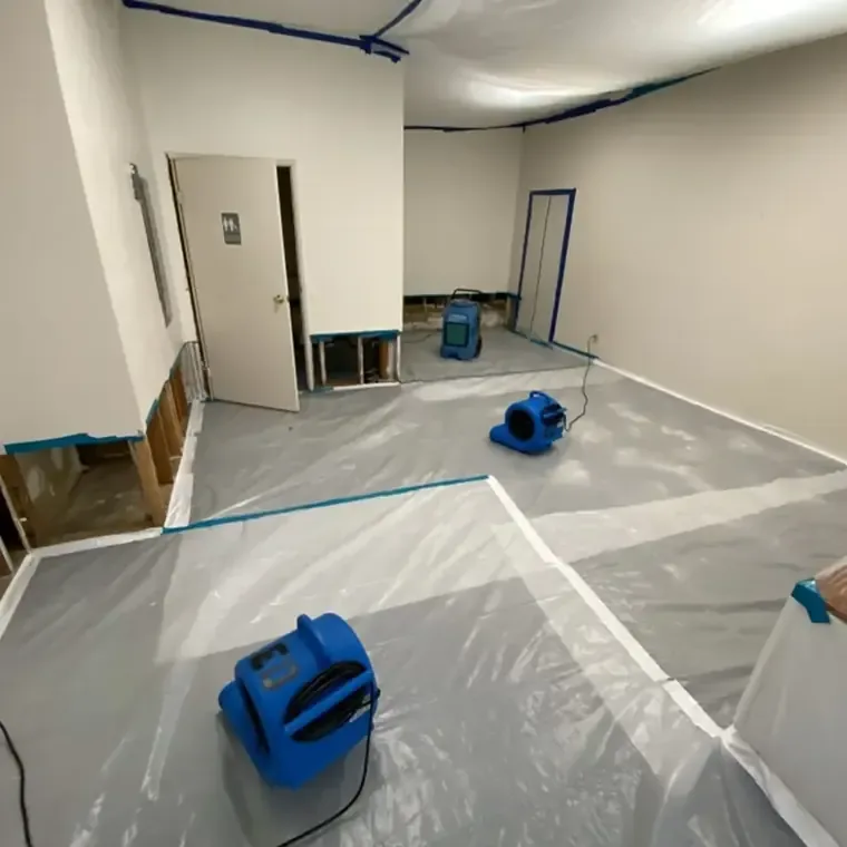 Blue air movers on a stripped floor inside plastic containment