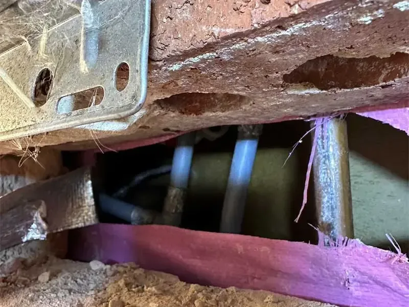 Wet crawl space under a raised wood floor with supply pipes and soil